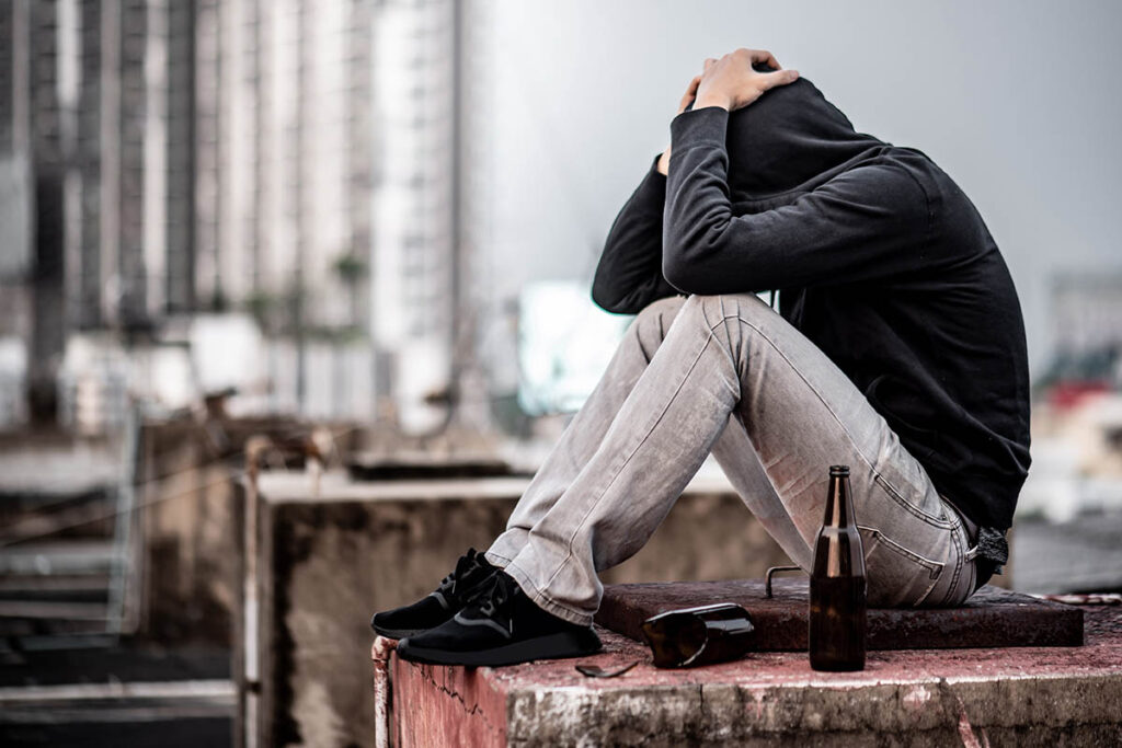 Troubled youth in a hoodie with his head in his hands in a grungy part of town