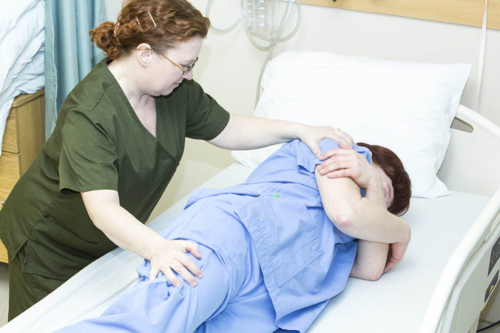 Health care aide assisting patient in hospital bed
