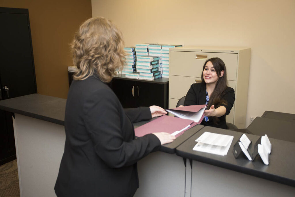 Administrative assistant handing folders full of paper to another person