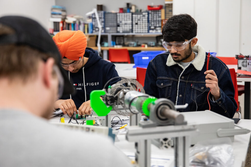 Three students working on electromechanical components in a mechatronics lab.