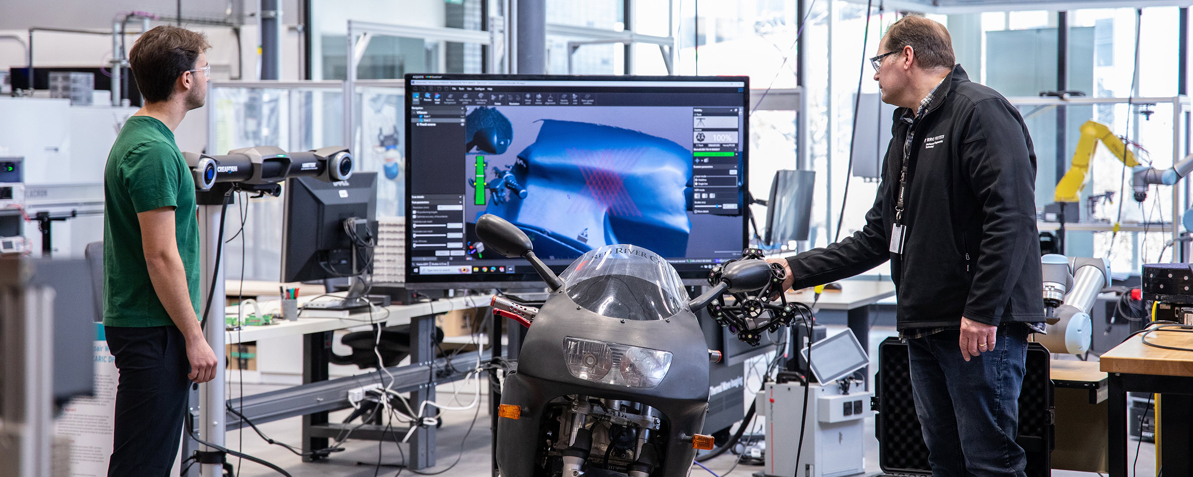 Student and instructor using a 3D scanner on a motorcycle in a shop environment.