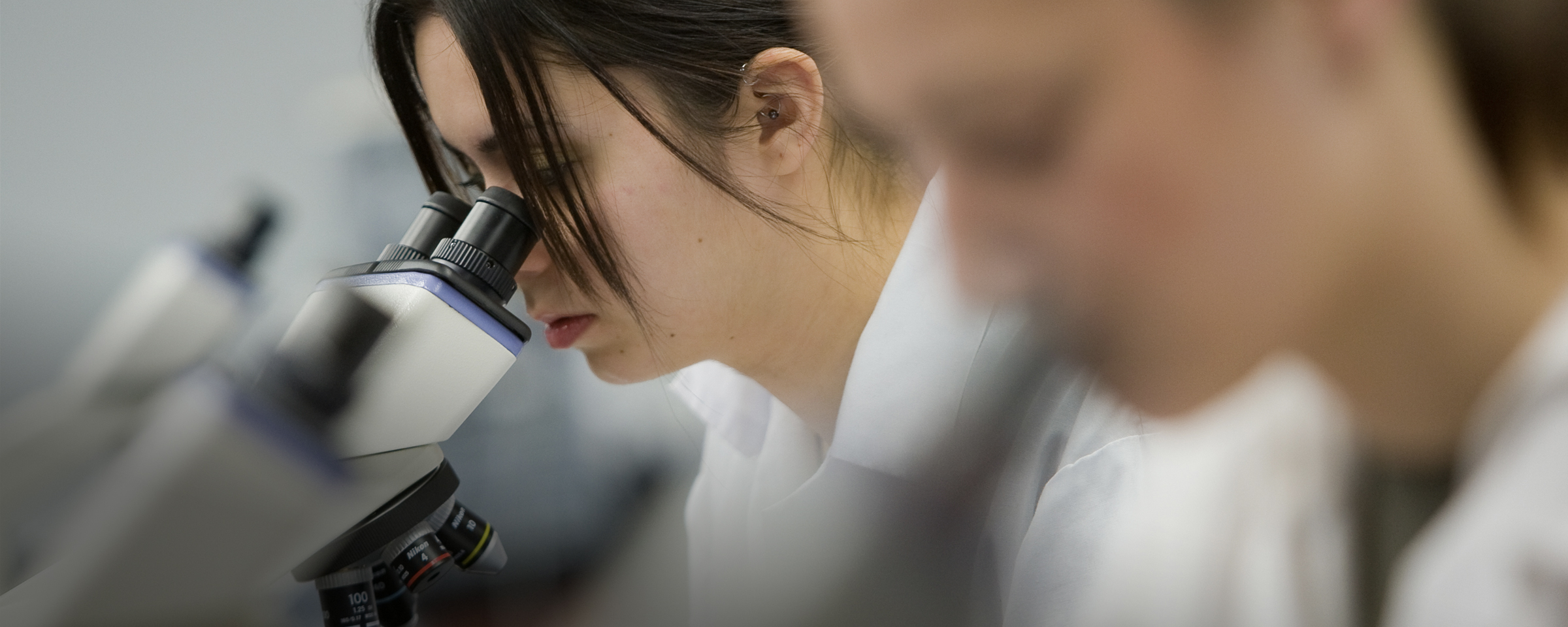 Students wearing lab coats and looking through microscopes